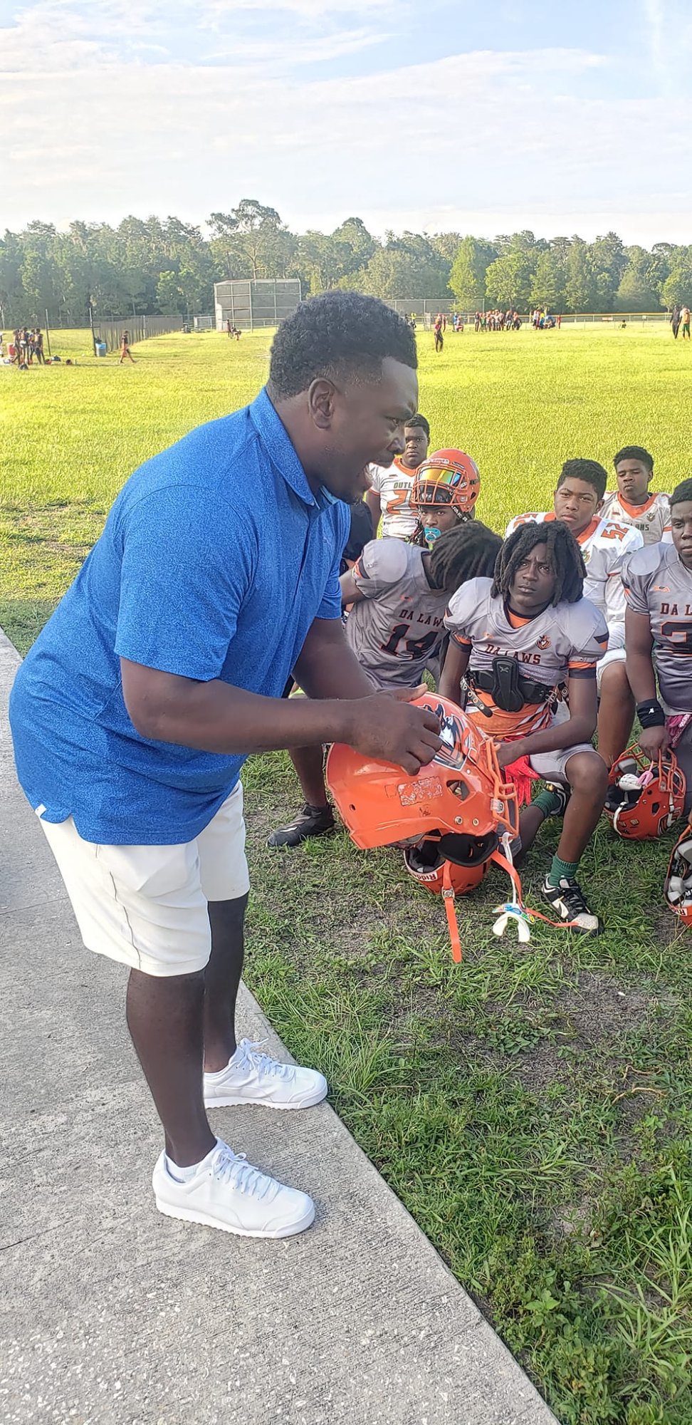 Coach BoJack leaning down speaking to seated youth football players